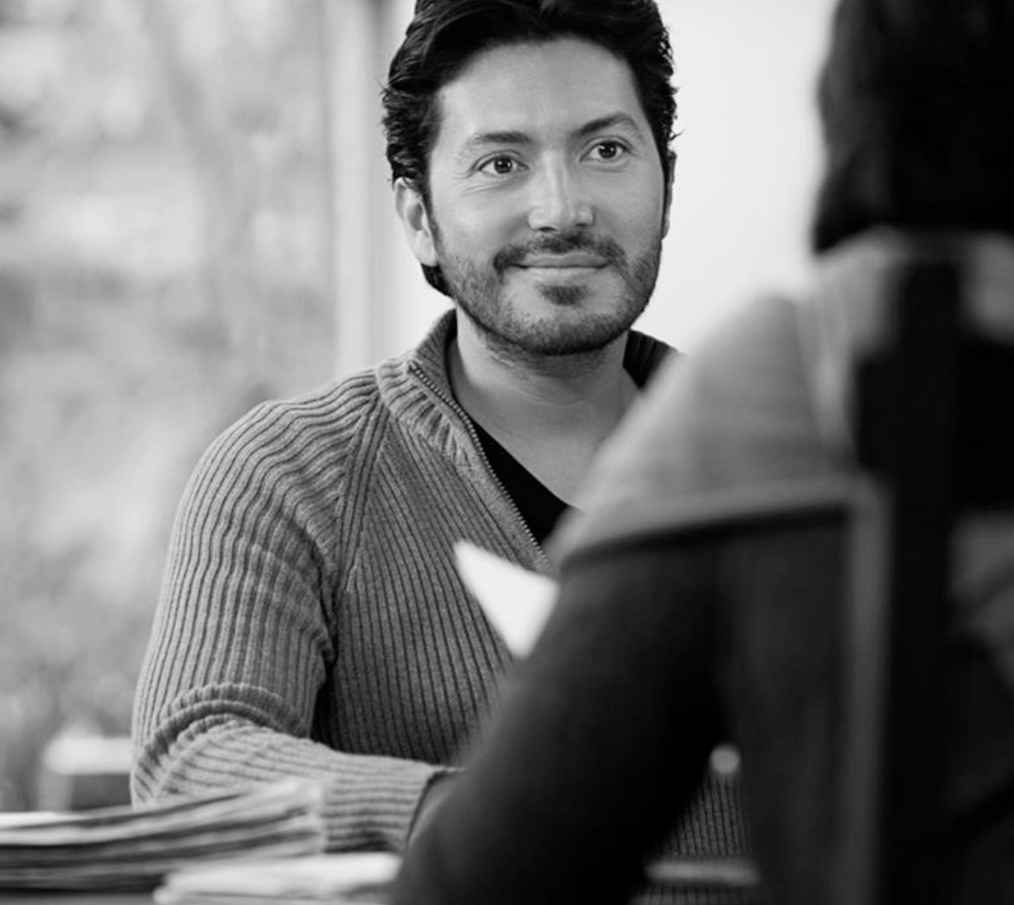 Man sitting facing a person holding a paper.